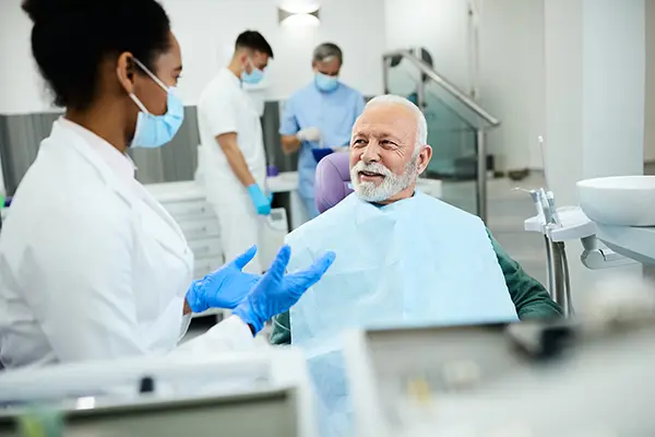 Older patient sitting in dental chair calmly discussing his oral health with dentist