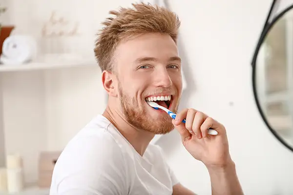 Smiling man brushing his teeth in a modern bathroom, promoting dental hygiene for a healthy smile.