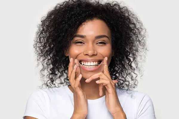 Smiling woman holding dental floss in her hands and demonstrating a proper flossing technique against a plain background.